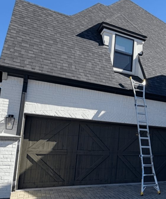 Two-story home with a ladder against the shingle roof above the garage