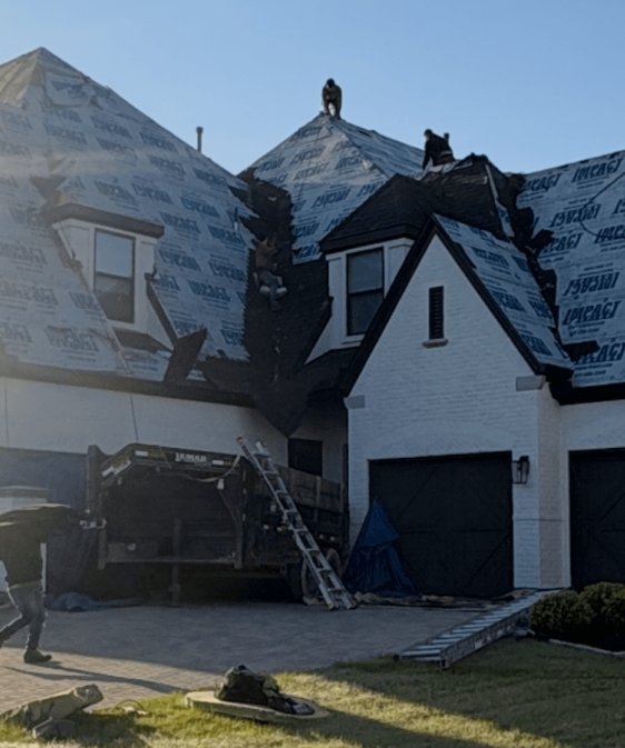 White brick home with a steep shingle roof and a ladder set up at the roof