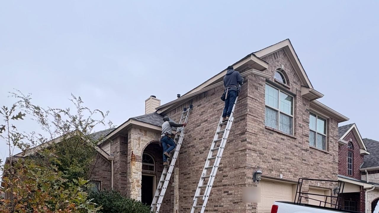 Different Roofing crew on ladders installing gutters on a two-story brick home
