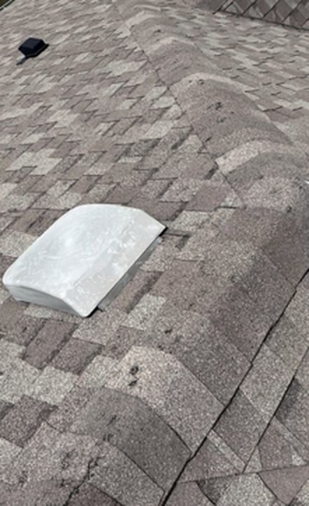 Hail-damaged asphalt shingles with granule loss next to a roof vent, photographed during a storm damage inspection